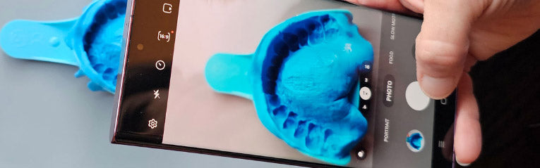Person using a smartphone to take a photo of a blue dental impression tray.
