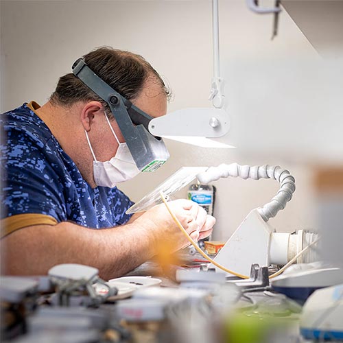 Person wearing a face mask and headlight working on a task with tools and equipment around.