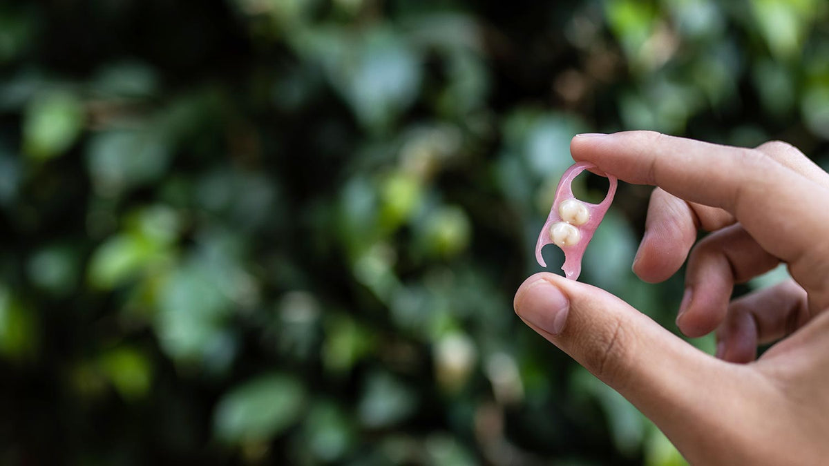 Hand holding a small pink tool with two beads against a blurred green background