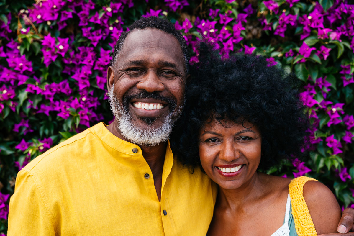 two older adults smiling and embracing with a floral background enjoying spring like weather