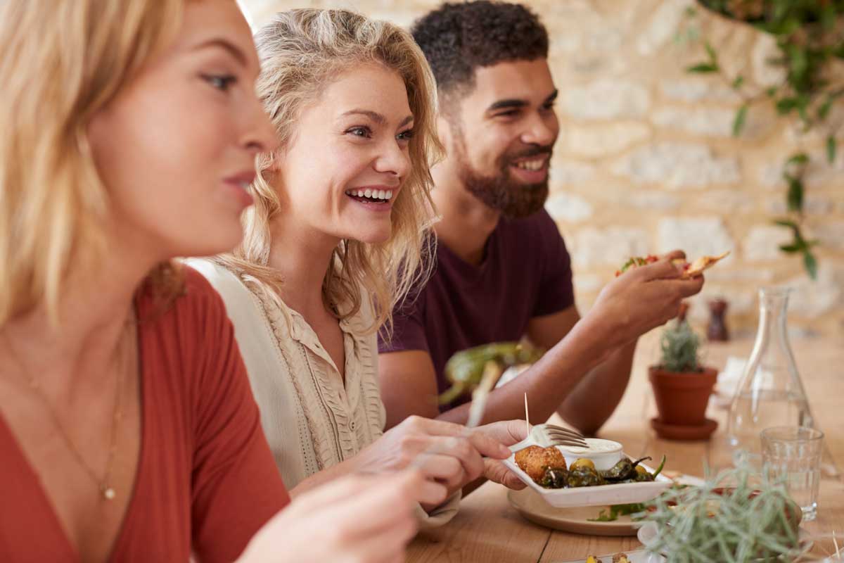 Group of friends sitting at a table, smiling and enjoying a meal together in a cozy setting with natural decor