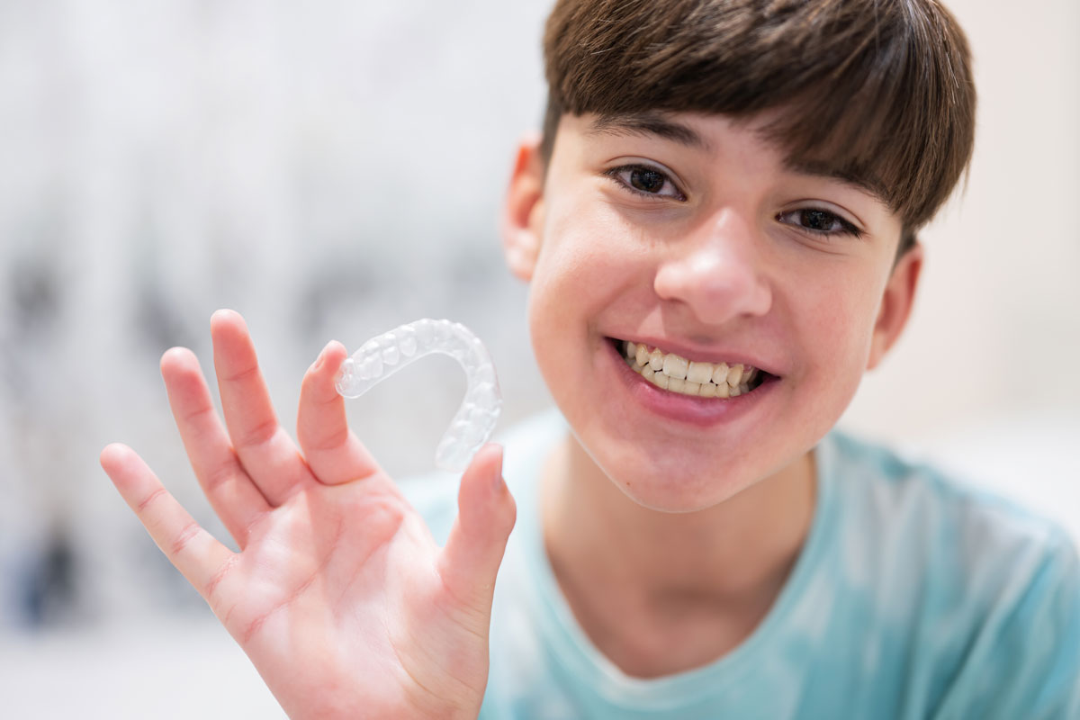 Smiling boy holding a clear dental retainer