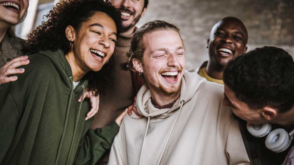  A group of five diverse friends sharing a joyful laugh together, each dressed in casual, comfortable clothing and clearly enjoying the moment