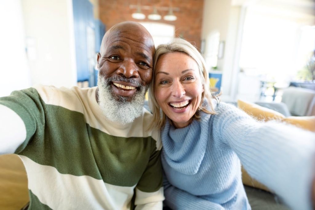 an older, interracial couple smiling while taking a selfie