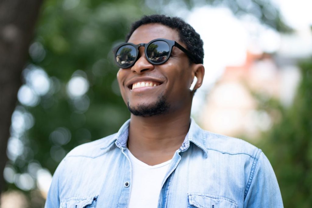 man wearing sunglasses and smiling while standing outdoors at the park. Partial dentures cost
