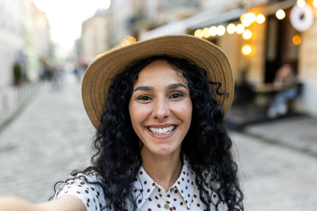A young woman wearing a hat, smiling while taking a selfie