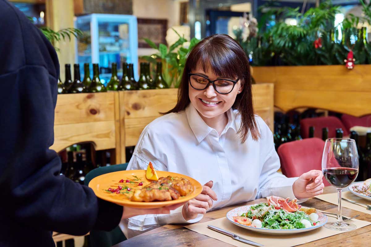 a woman smiling while being served dinner at a restaurant