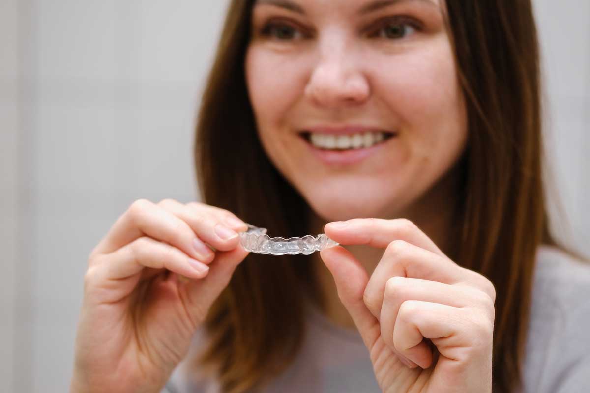 Close-up of a smiling woman holding a clear dental aligner in front of her, illustrating a focus on modern orthodontic solutions