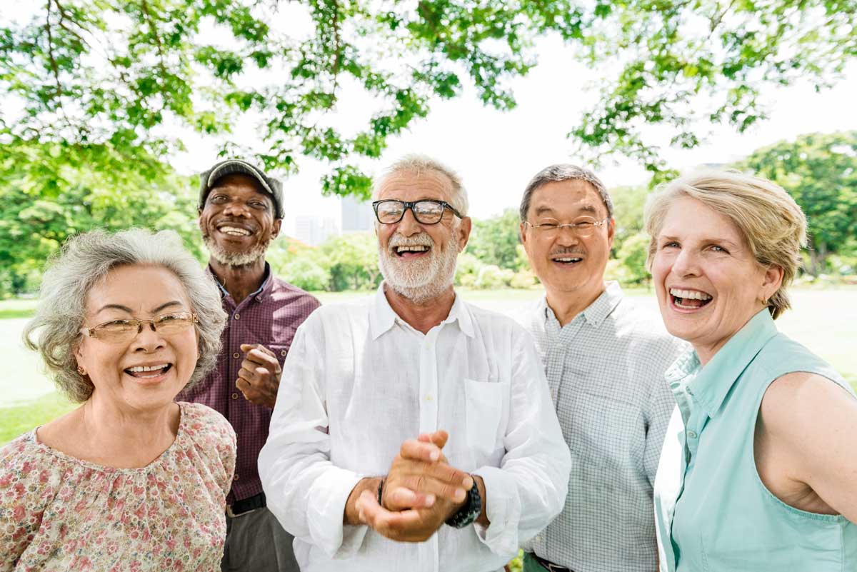 Group of five diverse senior friends laughing together in a sunny park, highlighting their joy and unity