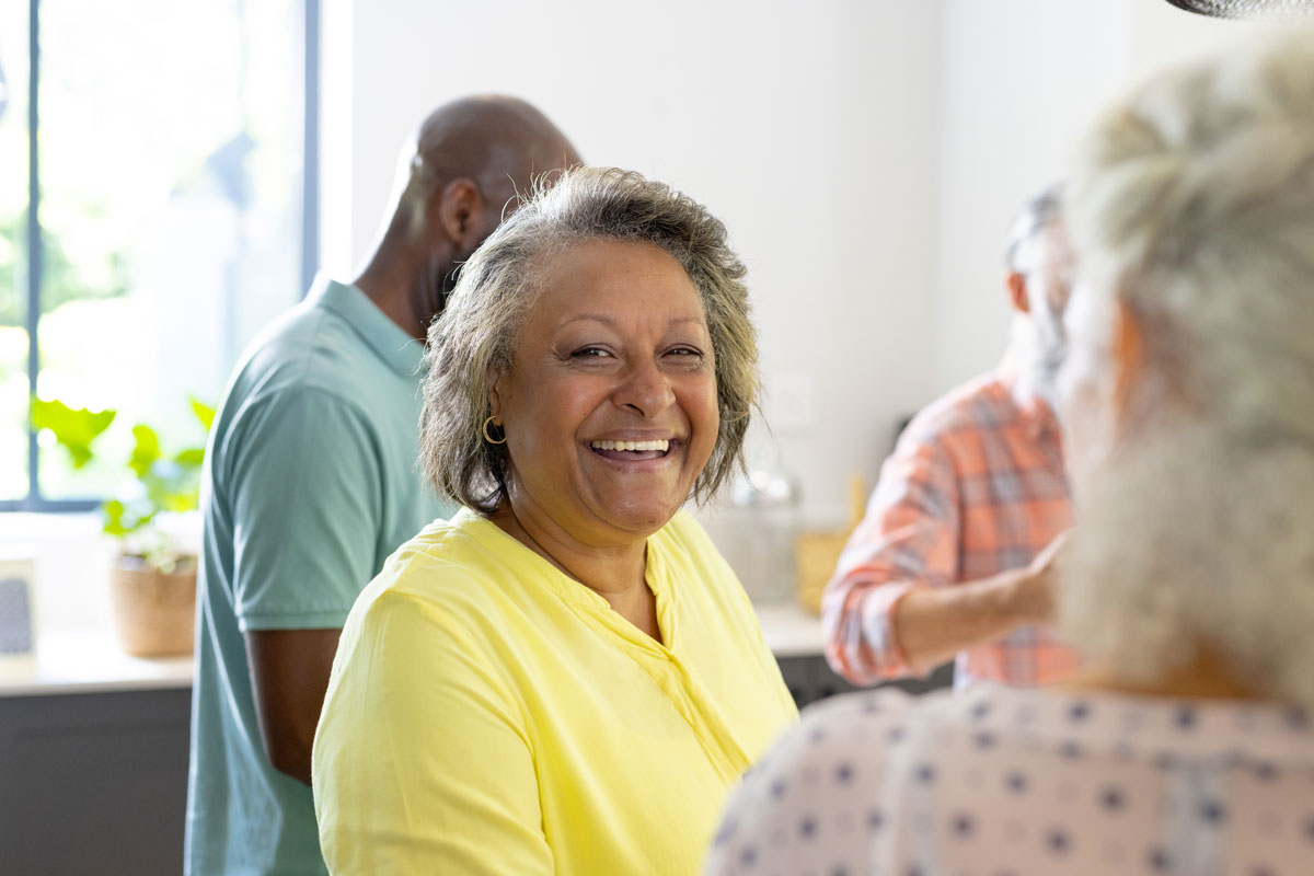 Smiling older woman in a bright yellow top enjoying conversation at a casual social gathering
