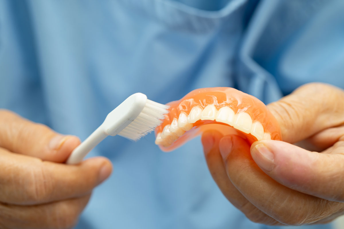 Close-up of a person cleaning a set of dentures with a toothbrush