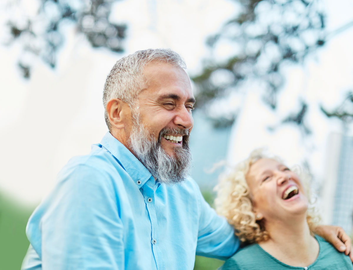 Smiling older couple laughing outdoors, enjoying a joyful moment together
