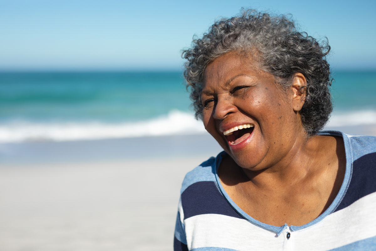Smiling older woman laughing on the beach with the ocean in the background