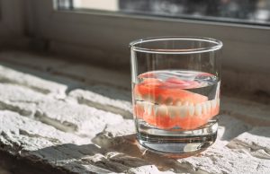 Dentures soaking in a glass of water placed on a sunlit windowsill