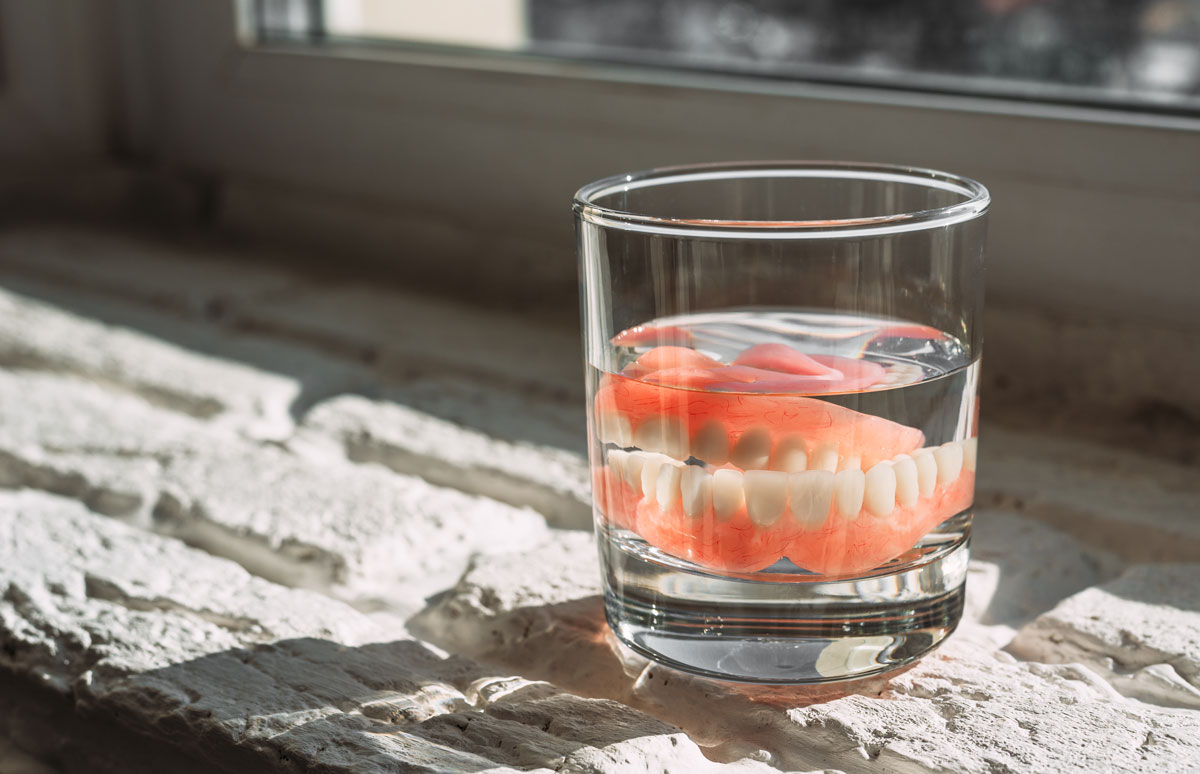 Dentures soaking in a glass of water placed on a sunlit windowsill
