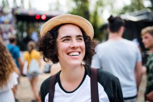 Person smiling and wearing a straw hat at an outdoor event with people in the background