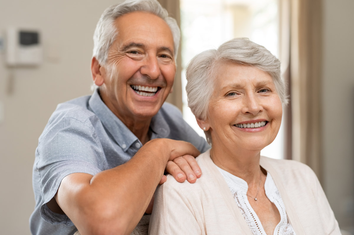 smiling older couple sitting together indoors, looking happy and relaxed
