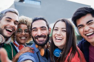 Group of five friends smiling and taking a selfie outdoors, wearing headphones around their necks
