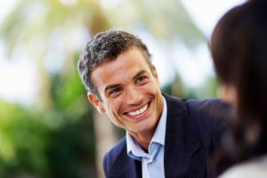 Man in a suit smiling warmly while talking to someone outdoors