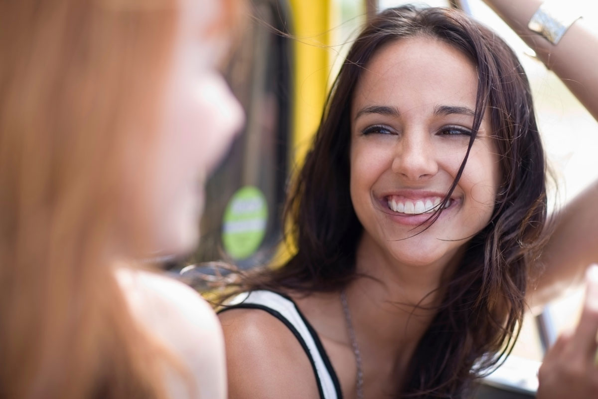 Woman smiling brightly while talking to a friend outdoors on a sunny day