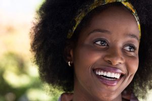 Close-up of a smiling woman with curly hair wearing a colorful headband and looking off to the side