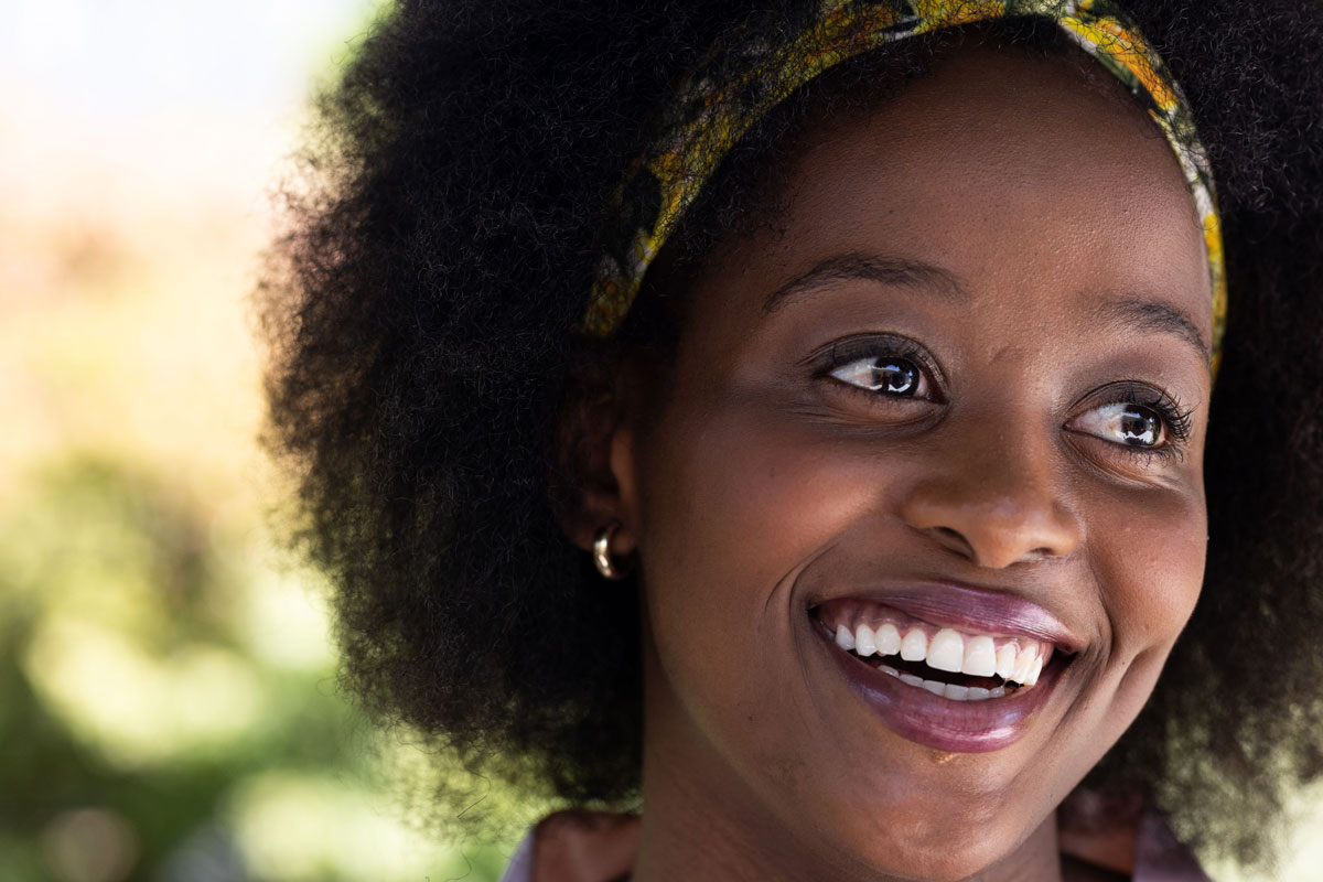 Close-up of a smiling woman with curly hair wearing a colorful headband and looking off to the side