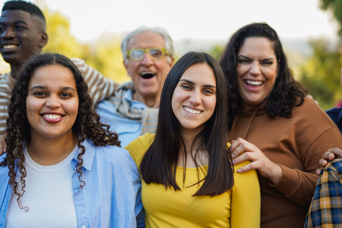 Group of people of different ages and backgrounds smiling and standing close together outdoors